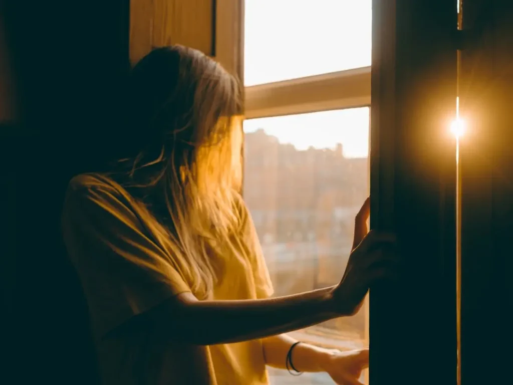 Silhouette d’une femme près d’une fenêtre, entre ombre et lumière, représentant la lutte contre l’anxiété, les peurs et la recherche d’apaisement.